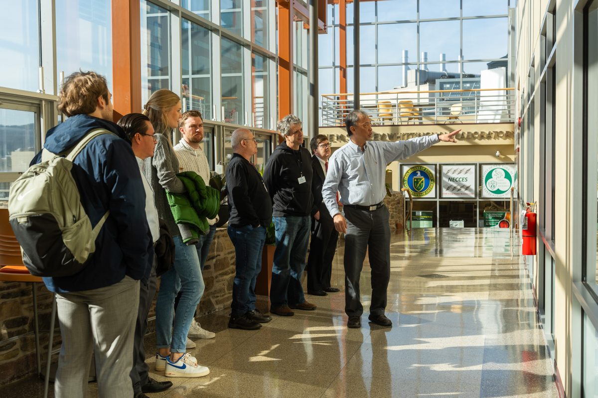 Students and faculty have a discussion in a hallway lined with large windows.